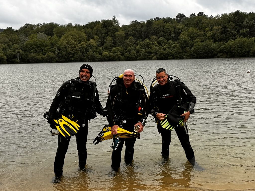 Trois plongeurs souriants au bord du lac, palmes à la main